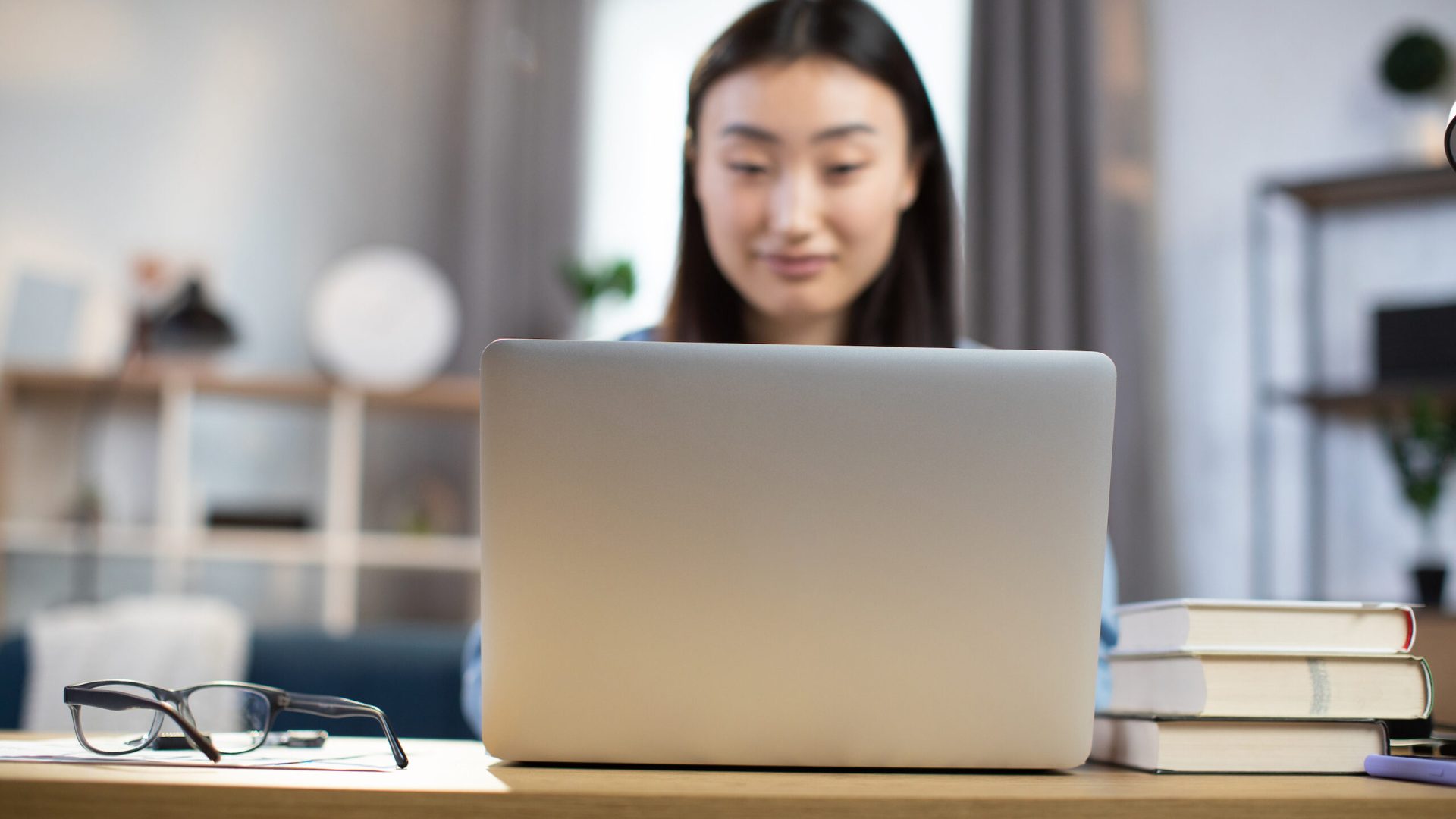 Blur background of young asian woman sitting at desk and surfing internet on portable computer. Focus on wireless laptop. Concept of freelance and technology.